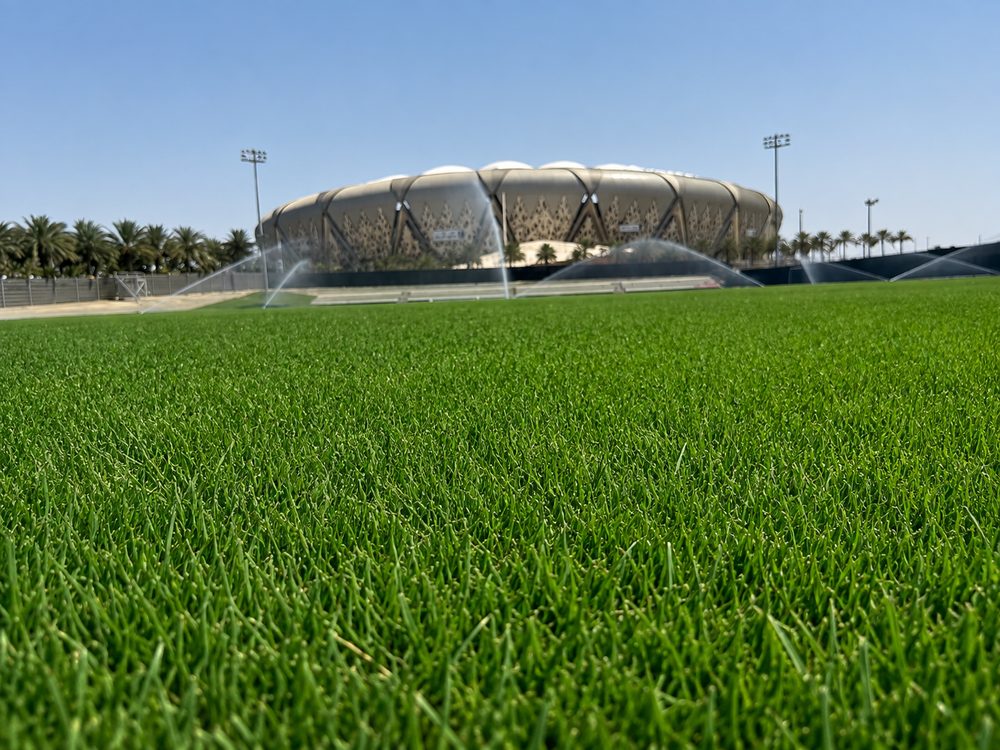 The playing surface being watered by automated sprinklers, main stadium beyond