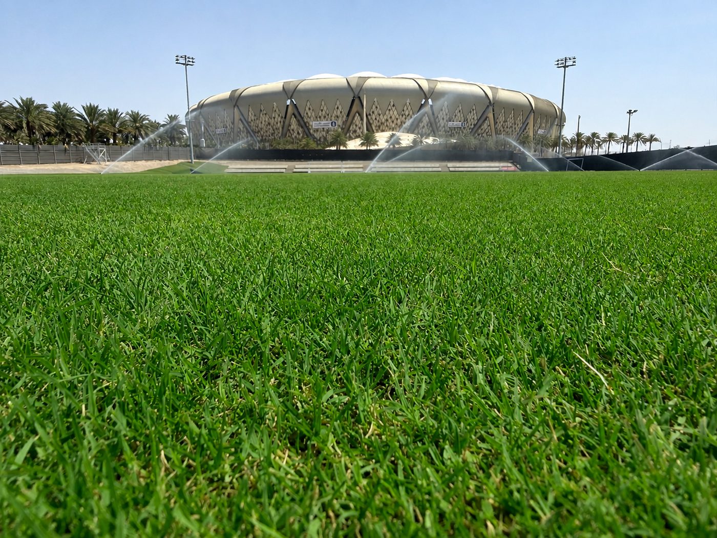 A full-size grass training pitch with the main stadium rising beyond