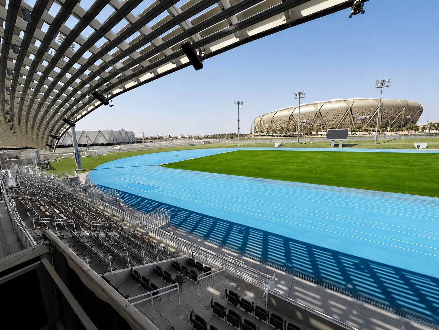 The full oval of the athletics track seen from beneath the shaded main stand, with the main stadium beyond